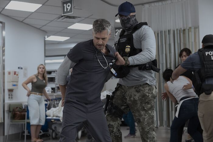 A tense scene from The Pitt Season 2 Episode 12 with a man in scrubs being restrained by an agent in a hospital setting.