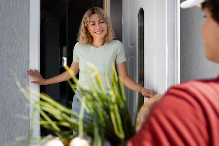 Woman smiling at front door as a neighbor delivers fancy wedding invites after repeated misdelivery issues.