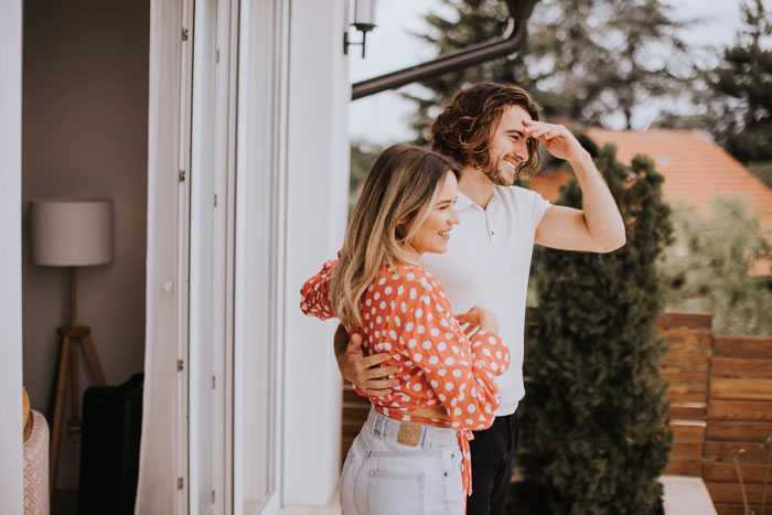 Couple standing on porch smiling as they expect help with misdelivered fancy wedding invites from a neighbor nearby