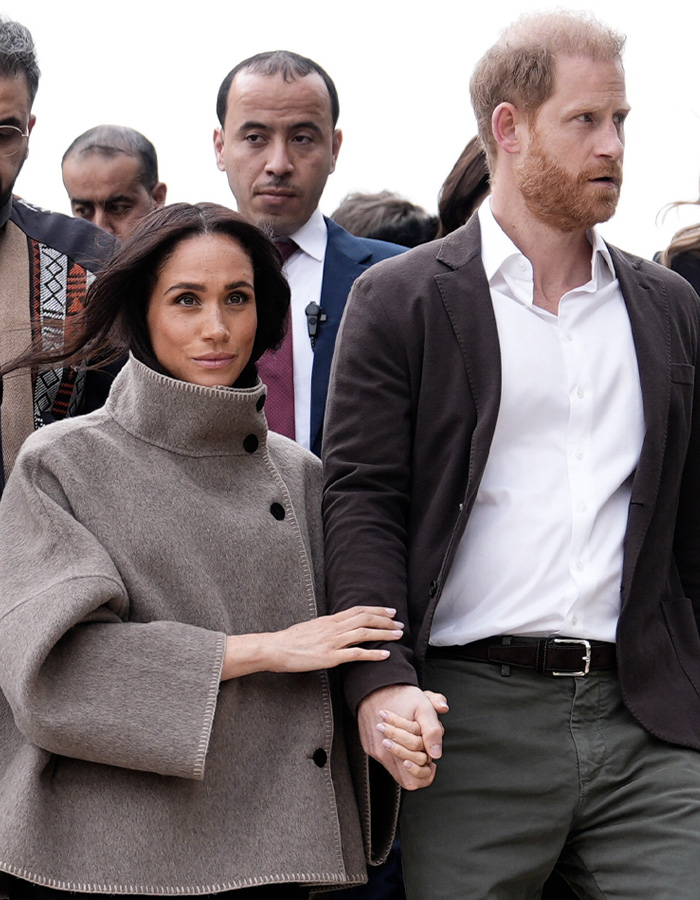 Meghan Markle and Prince Harry walking outdoors with security, reflecting Netflix cuts ties affecting struggling As Ever brand.