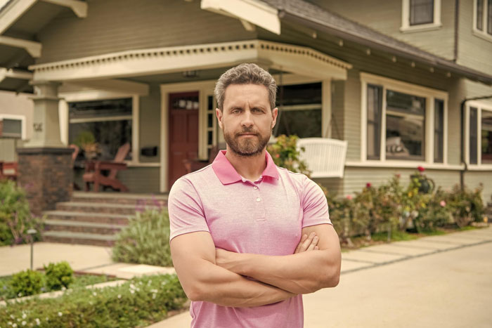 Man standing with arms crossed outside his home focused on neutering neighbor cat stray concerns in a suburban setting