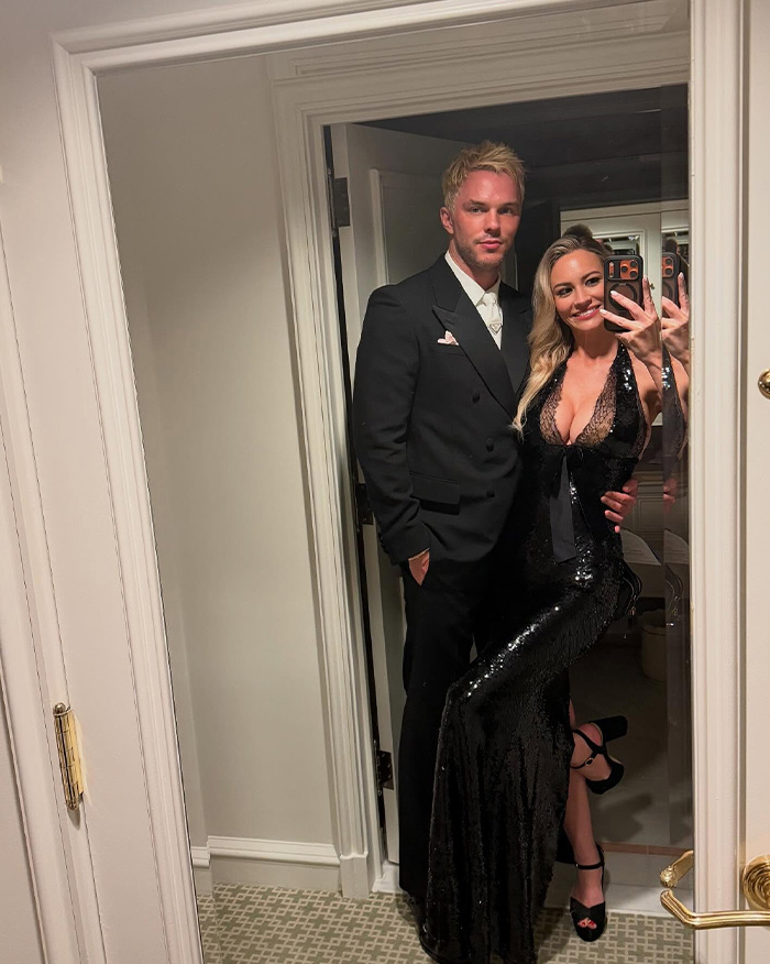 Bryana Holly and husband Nicholas Hoult in formal attire posing for a mirror selfie at Oscars party confident against body-shaming.