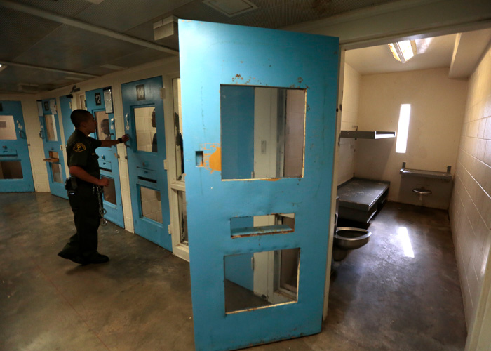 Prison officer opening a cell door showing a sparse room, reflecting breaking point signs and alarming conditions.