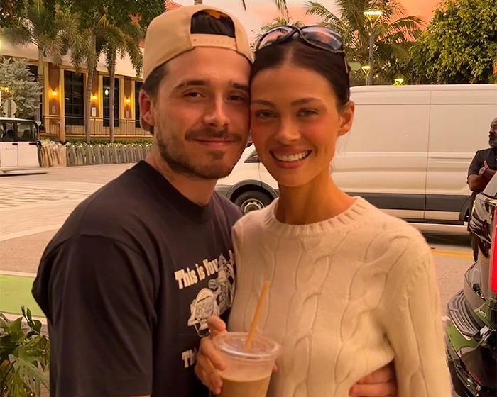 Brooklyn Beckham and Nicola Peltz smiling outdoors, with Nicola holding a cold drink, casual and relaxed atmosphere.