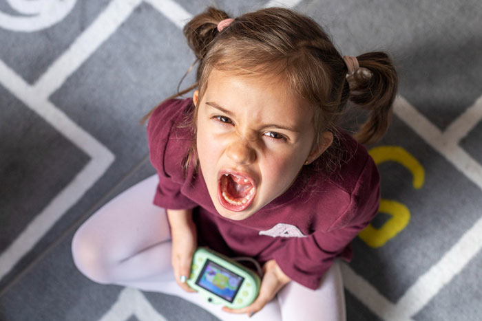 Angry young girl with pigtails shouting while holding a handheld gaming device, illustrating violent niece behavior concept.