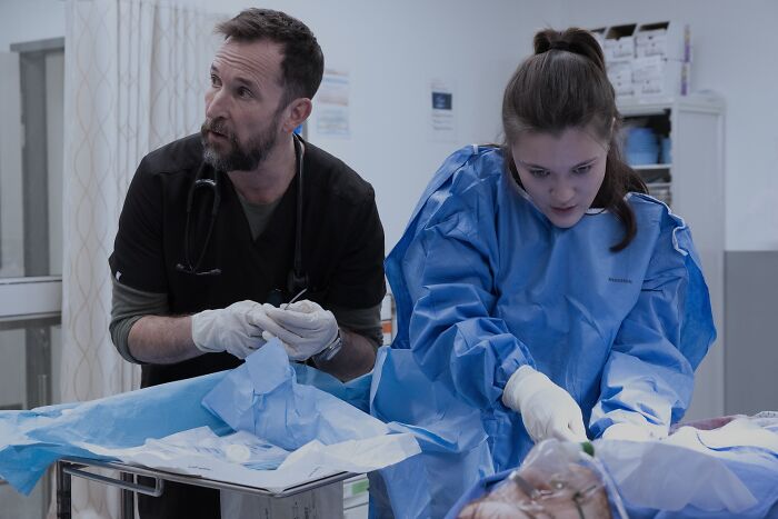 Two medical professionals in protective gear performing a procedure in The Pitt Season 2 Episode 13 preview scene.