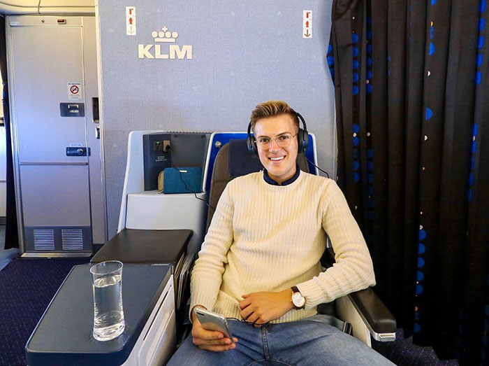 Influencer sitting in airline business class seat wearing headphones and holding phone, avoiding economy class flight.