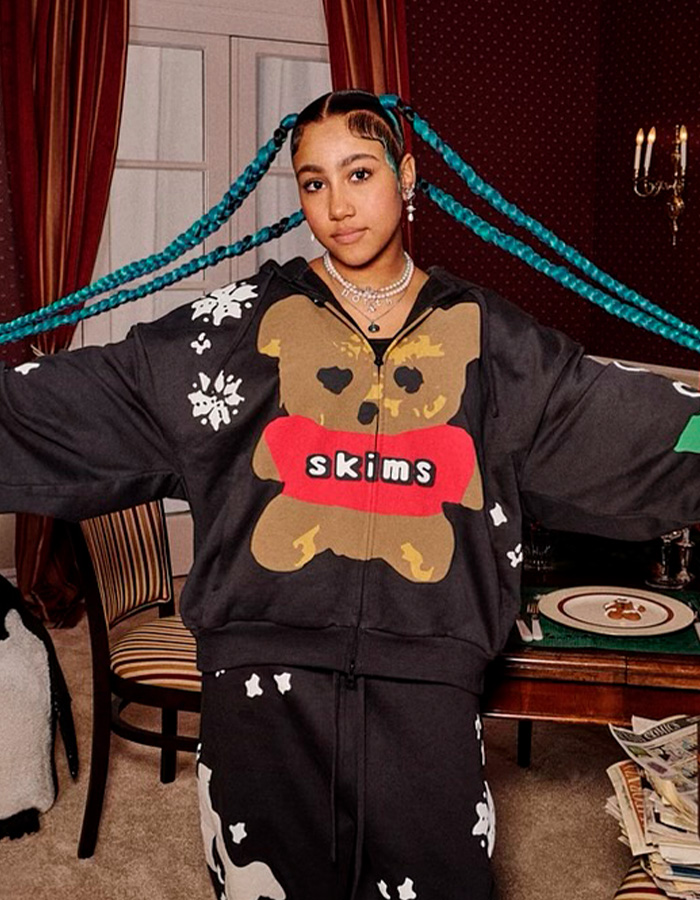 Young woman with long turquoise braids wearing a black skims outfit, showing off her spiked pierced manicure trending online.