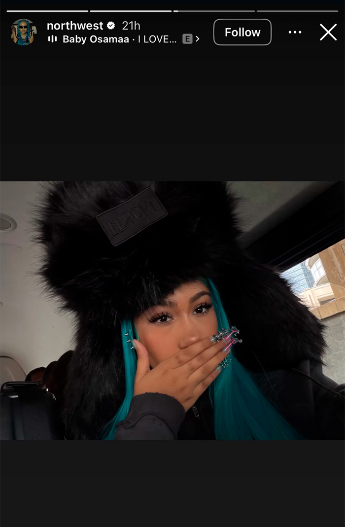 Teen girl with blue hair wearing a black fur hat, showing off her spiked and pierced manicure in a car interior.
