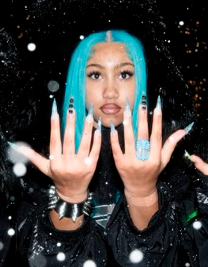 Young woman with vibrant blue hair showing off spiked pierced manicure with long nails and rings in a night setting.