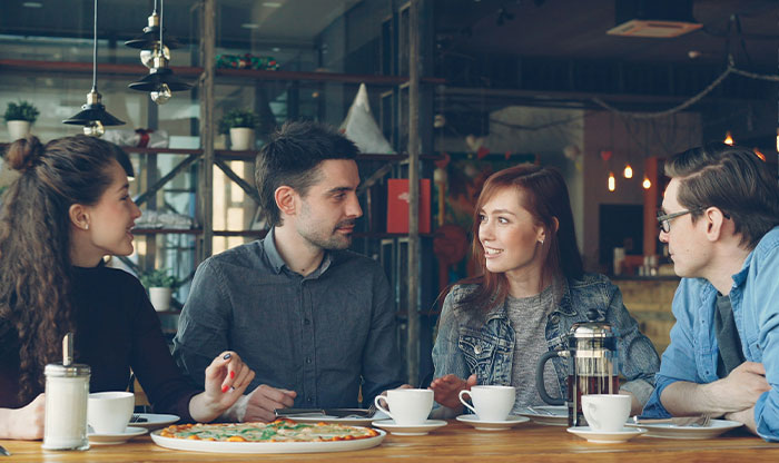 Four friends having coffee and pizza in a cozy cafe, illustrating themes of privilege and social interaction.