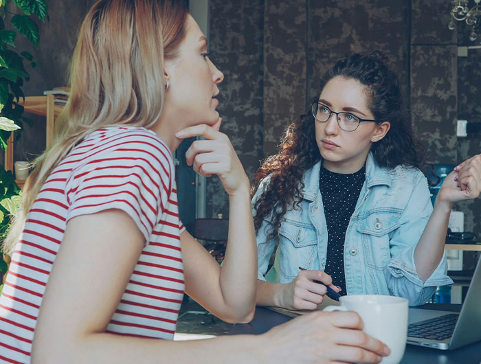 Two women having a serious conversation indoors, highlighting themes of privilege and social disconnect.