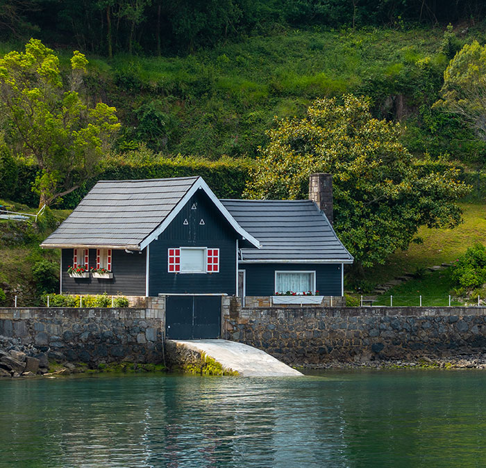 Cozy house by water reflecting a green hillside, illustrating a bride's harsh reality check about honeymoon at sibling’s house. Cozy house by water reflecting a green hillside, illustrating a bride's harsh reality check about honeymoon at sibling’s house.