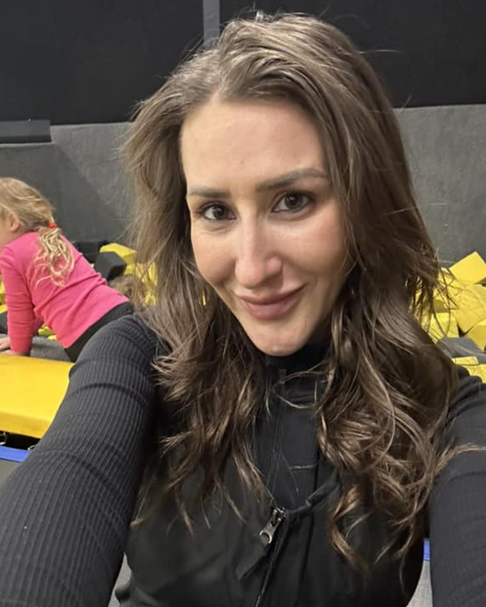 Woman with long brown hair smiling in a black top with nurse's chilling final text revealed after ex-coworker arrest background.