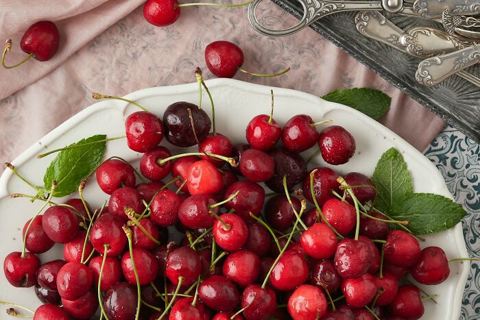 Fresh cherries with water droplets on a white plate surrounded by vintage silverware and a pink cloth, highlighting dumb ER visits.