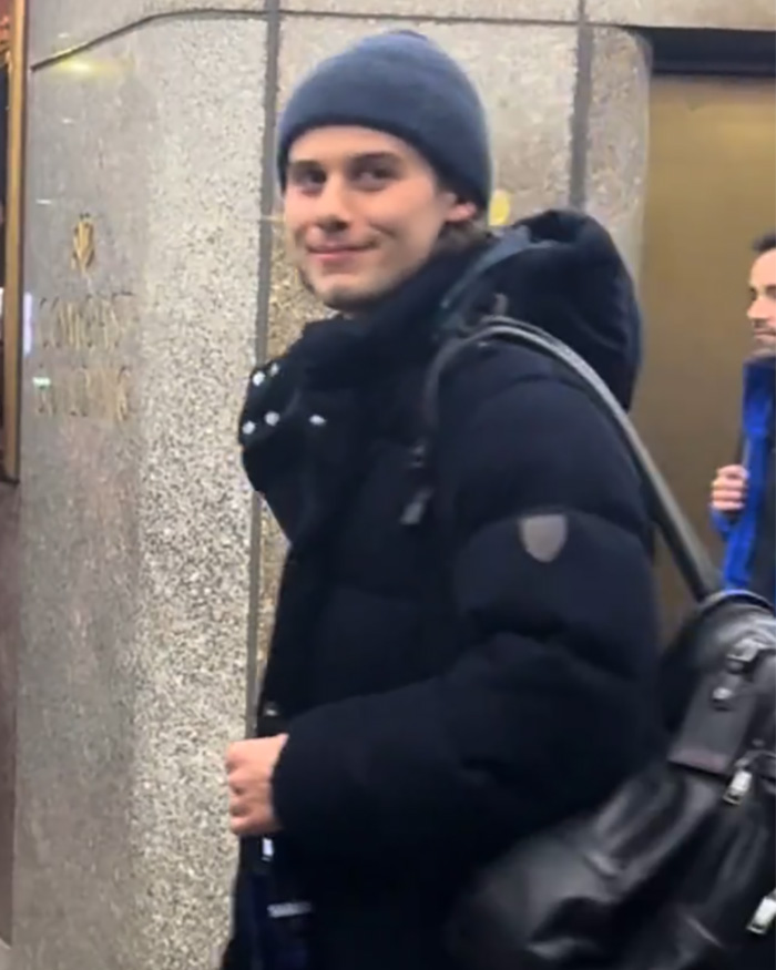 Olympic hero Jack Hughes in a black jacket and beanie awkwardly interacting with a crowd on a city street. Olympic hero Jack Hughes in a black jacket and beanie awkwardly interacting with a crowd on a city street.
