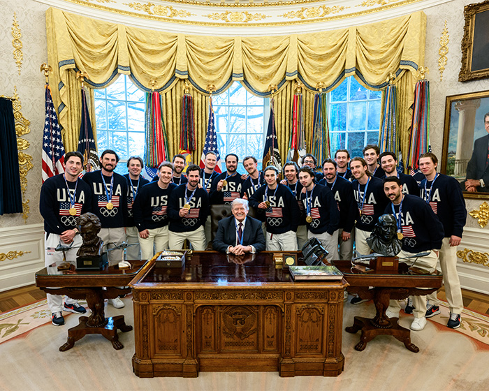 Olympic hero Jack Hughes with USA Olympic team members posing in the Oval Office wearing medals and team sweaters. Olympic hero Jack Hughes with USA Olympic team members posing in the Oval Office wearing medals and team sweaters.