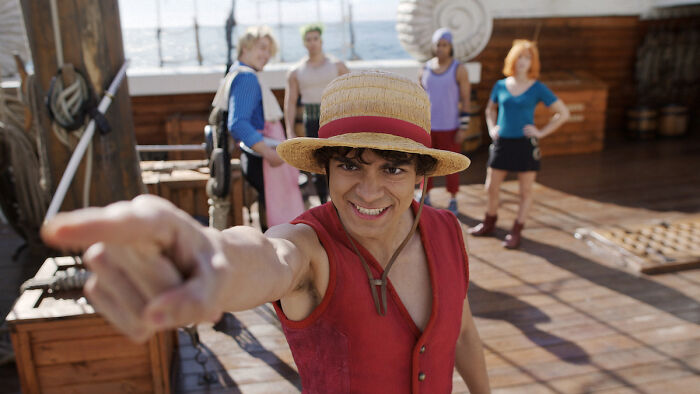 Main characters from One Piece anime aboard a ship, focusing on a smiling young man wearing a straw hat.