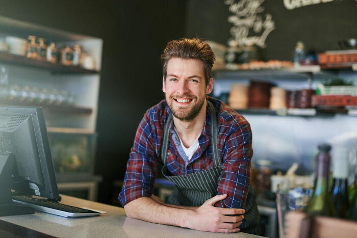 Smiling barista leaning on counter in coffee shop, representing savage I literally own the company moments witnessed by people.