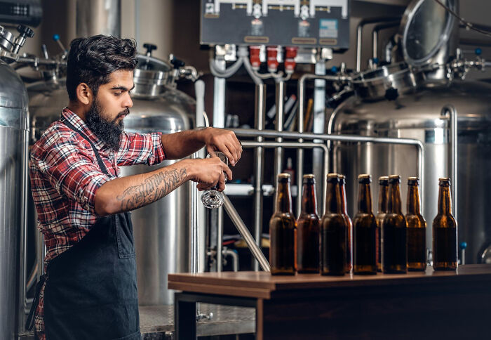 Man in brewery pouring beer into glass bottles, showcasing confident ownership in a craft brewing company setting.