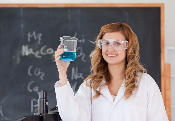 Young scientist in lab coat and goggles holding a beaker with blue liquid, showcasing savage company moments.
