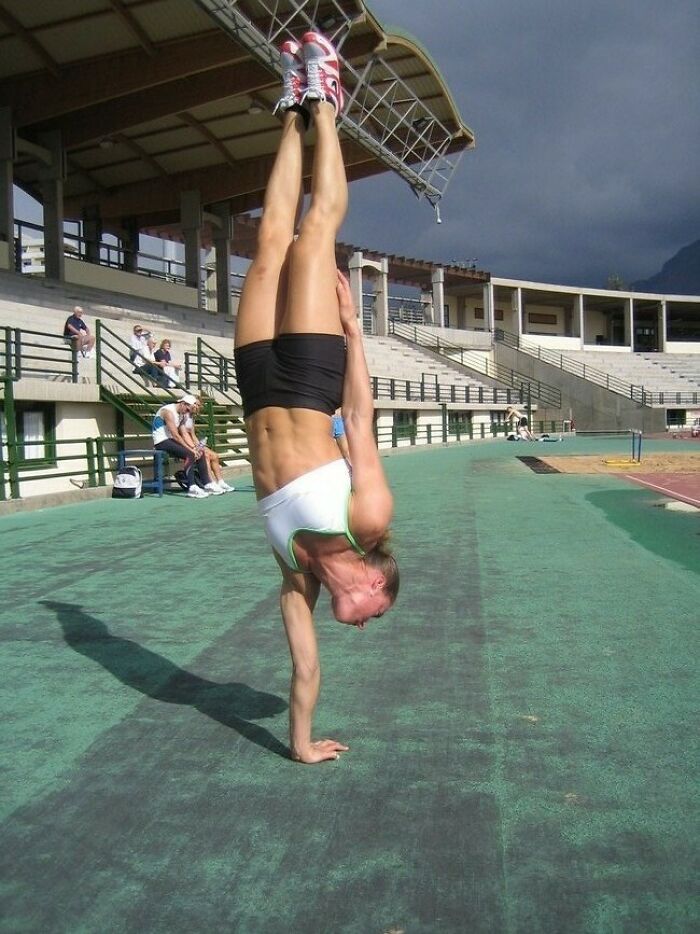 Woman performing a one-handed handstand on an outdoor track, showcasing strength and balance in athletic wear.