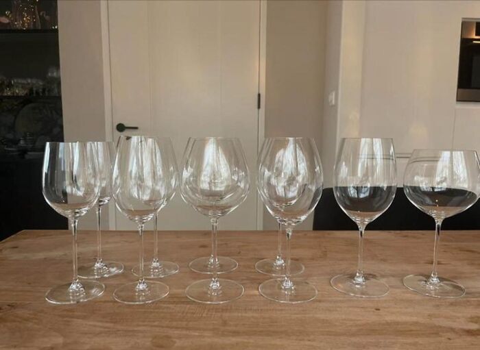 Eight empty wine glasses arranged on a wooden table, showcasing a bizarre encounter with unusual glass shapes.