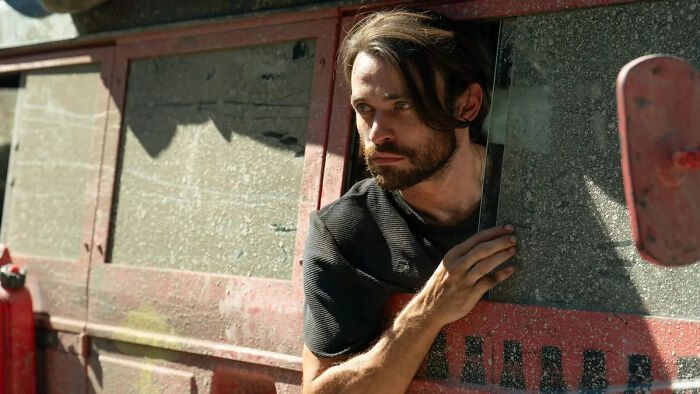 Man peeking cautiously from a dusty vehicle, illustrating the Paradise season 2 finale&rsquo;s most confusing twist explained by creators.