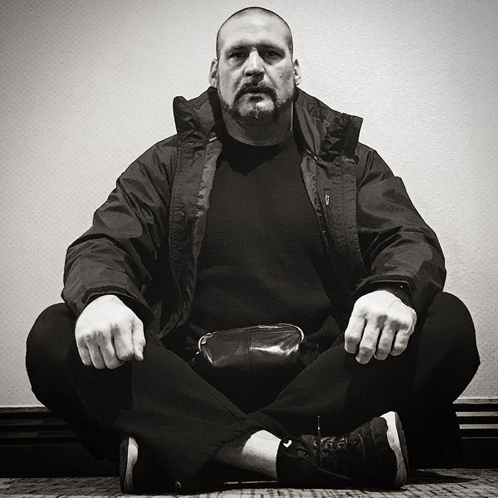 Security guard at the center of Chappell Roan and Jude Law's daughter debacle sitting cross-legged, wearing black jacket and sneakers.