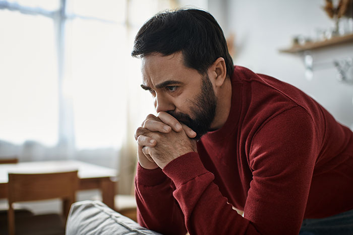 Man in a red sweater looking worried and deep in thought, doubting paternity of his 12-year-old son.
