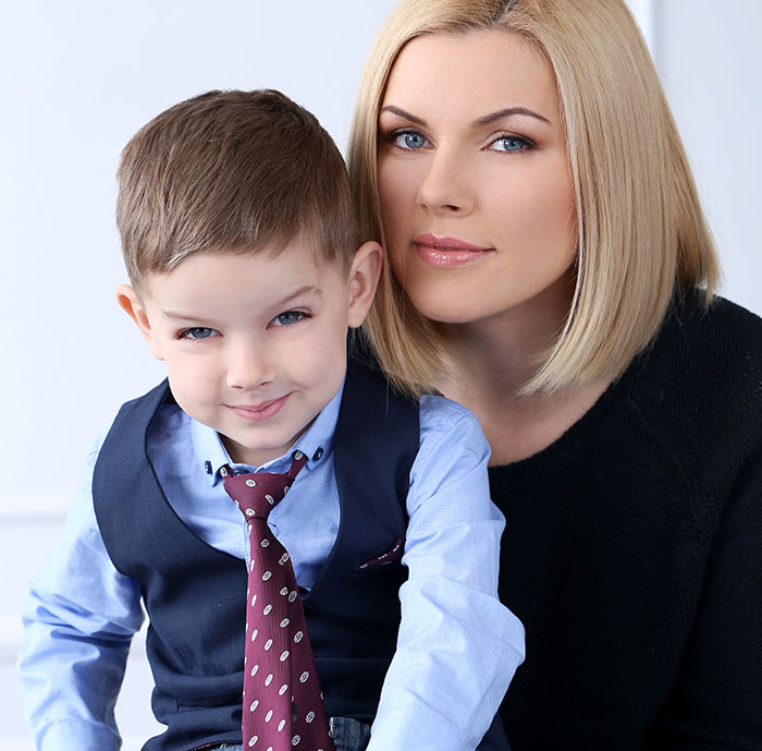 Woman with blonde hair sitting close to her young son wearing a vest and tie, hinting at dad doubting paternity.