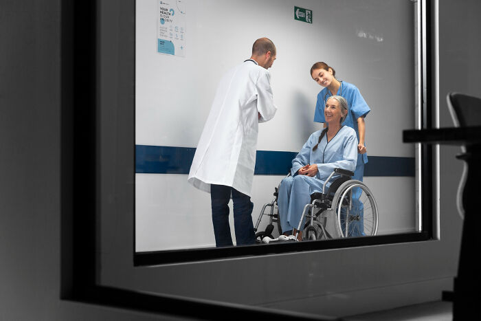 Surgical staff caring for a patient in a wheelchair, discussing unhinged patient confessions under sedation in hospital hallway.