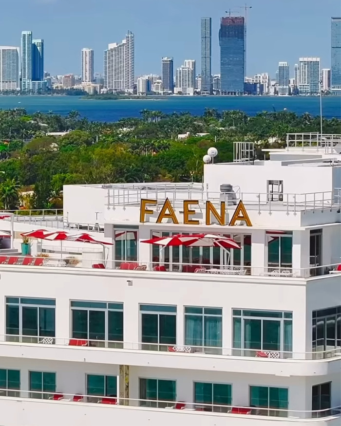 Faena hotel rooftop with red umbrellas, ocean view, and city skyline in the background in a sunny setting.