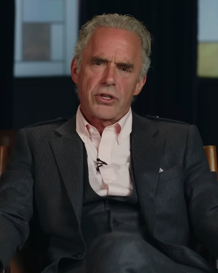 Man in dark suit and pink shirt speaking during an indoor interview about Pedro Pascal controversy and rumored boyfriend.