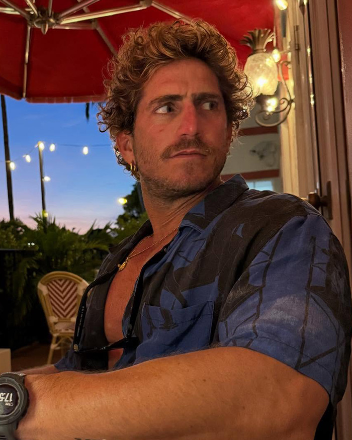 Pedro Pascal sitting outdoors in a casual shirt with curly hair during evening light, facing sideways with a thoughtful expression.