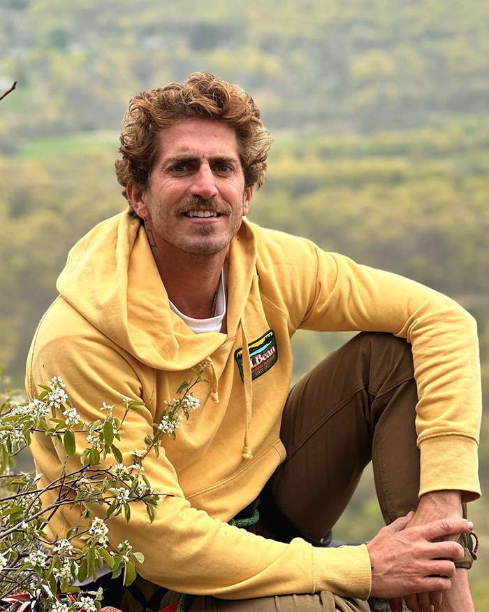 Man in yellow hoodie sitting outdoors surrounded by greenery, unrelated to Pedro Pascal blocking fans controversy.