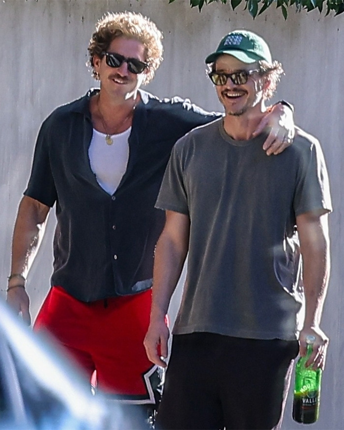 Two men wearing sunglasses, one with arm around the other, smiling outdoors in casual clothing.
