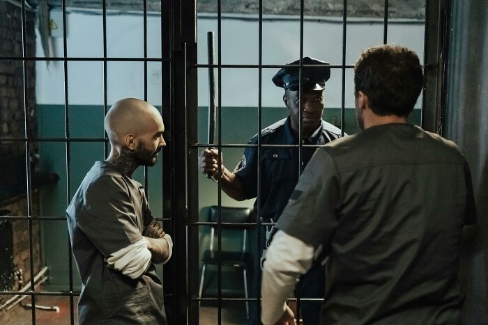 Two criminals in prison uniforms talking to a police officer behind bars illustrating crime cover up mistakes.