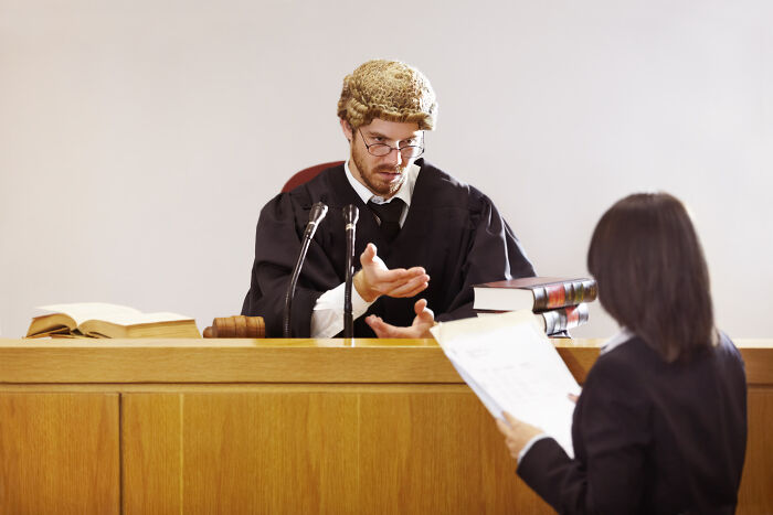Judge in traditional wig speaking to lawyer in courtroom, symbolizing criminals trying to cover up their crimes in dumb ways.