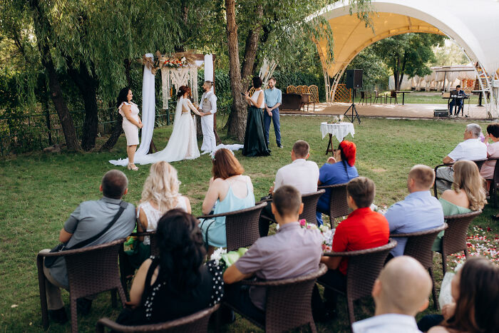 Outdoor wedding ceremony with guests seated, bride and groom exchanging vows under decorated arch, relating to petty grudges concept.