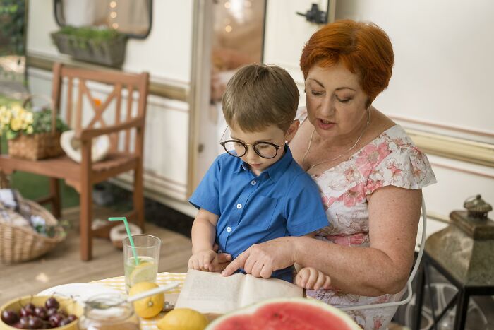 Older woman and young boy reading a book together, illustrating how people remember old petty grudges against strangers.