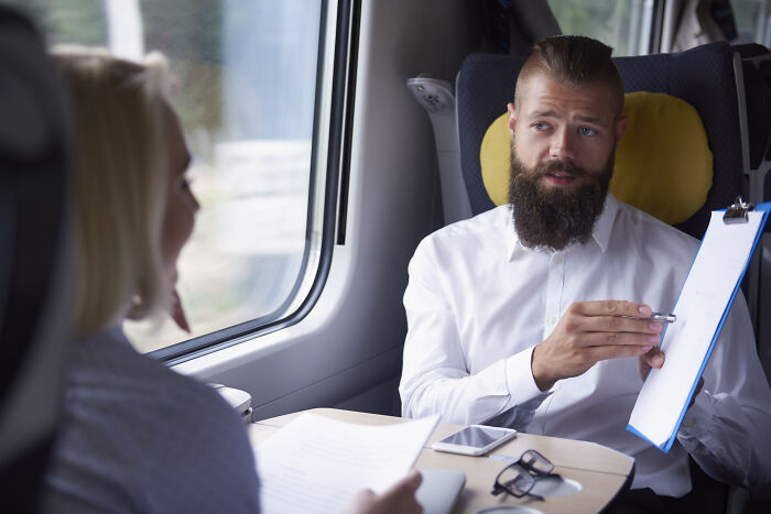 Man with beard holding clipboard talking to woman on train, illustrating petty grudges against strangers concept.
