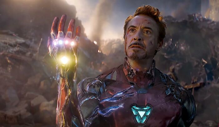 Iron Man in battle-worn suit, holding glowing Infinity Gauntlet, symbolizing old petty grudges against strangers.