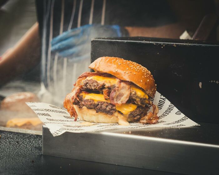 Double cheeseburger with bacon on sesame bun served at a smoky grill, illustrating a disastrous first dates food fail scenario.