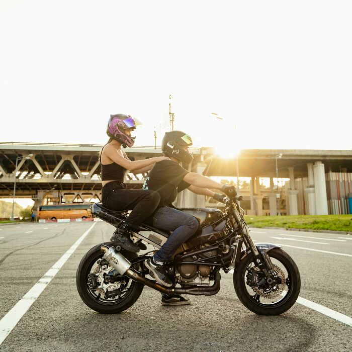 Couple riding a motorcycle wearing helmets during a sunset, illustrating a potentially disastrous first date experience.