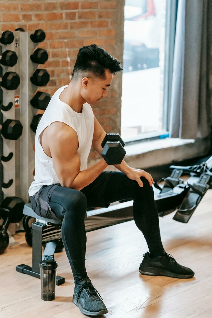 Man lifting dumbbell sitting on bench in gym, demonstrating serious strength and fitness training intensity.