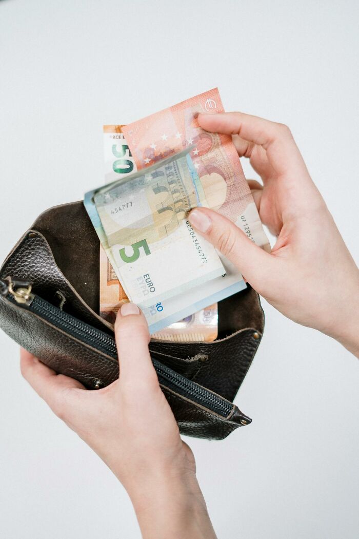 Person holding and counting euro bills from a black leather wallet, illustrating bizarre true stories involving money.