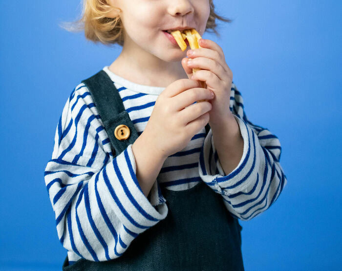 Child in striped shirt eating fries, capturing a wholesome moment of dads having their kids’ backs.
