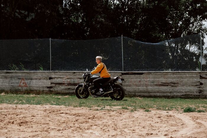 Person in an orange jacket riding a black motorcycle near a wooden fence, evoking challenges medical staff face in the ER.