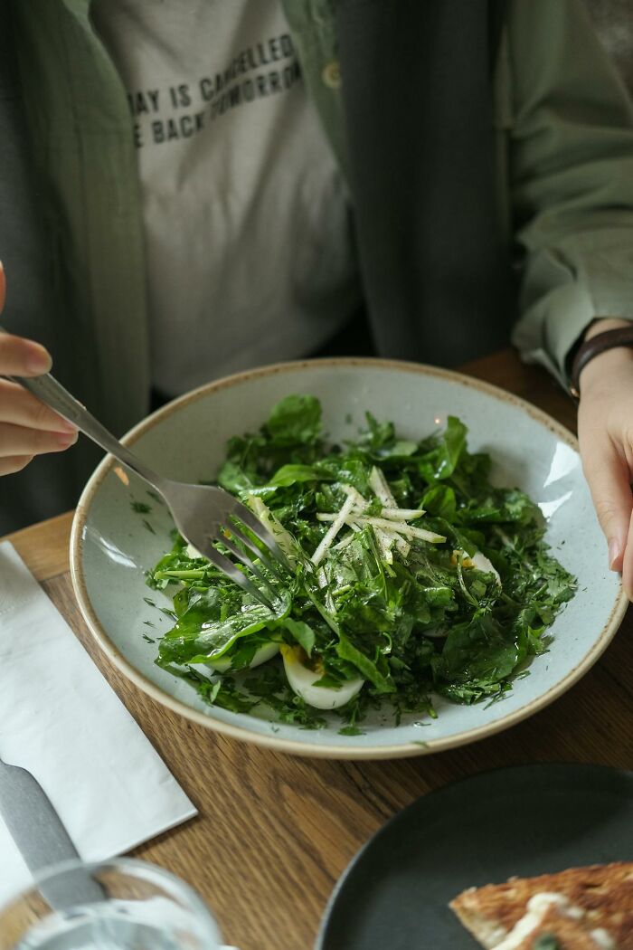 Person having a green salad with fresh herbs and eggs, illustrating disastrous first dates and awkward dining moments.